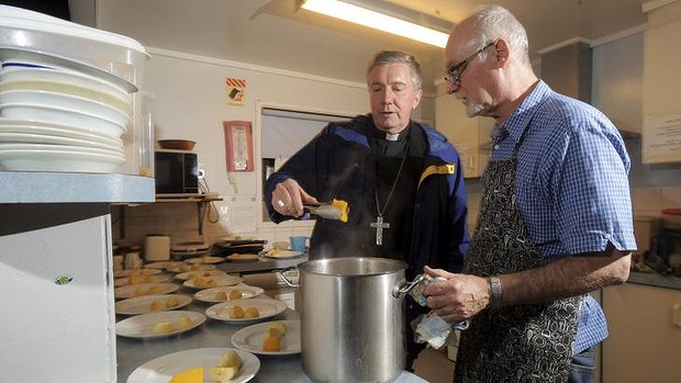 Catholic Archbishop of Canberra and Goulburn Christopher Prowse helps to dish out meals at the St Vincent de Paul Society's , Samaritan House Men's Shelter at Hackett. Cook John Barr is in the kitchen with him. Photo: Graham Tidy