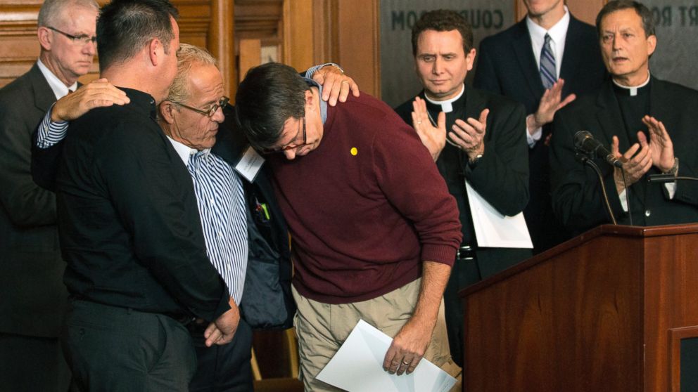 Attorney Jeff Anderson gives a hug to abuse survivors Jim Keenan, left, and Al Michaud, in red, after they both spoke of the importance of this historic agreement during a news conference in St. Paul, Minn., Monday, Oct. 13, 2014. A Minnesota judge... View Full Caption