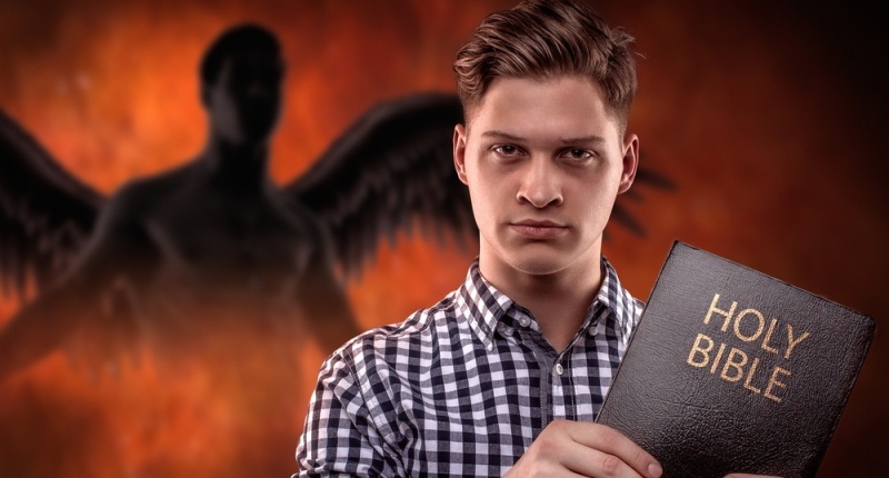 A man holds a Bible; hell fire rages in the background (Shutterstock)