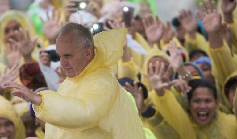 Pope Francis (L) wears a plastic poncho as he waves to well wishers after a mass in Tacloban on January 17, 2015. Pope Francis will spend an emotional day in the Philippines on January 17 with survivors of a catastrophic super typhoon that claimed thousands of lives, highlighting his concern over climate change.