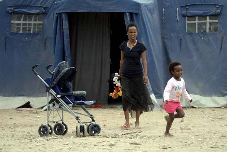 A migrant and her child stand next to a tent set up by the Red Cross in a refugee camp next to the Tiburtina train station in Rome on June 16, 2015.