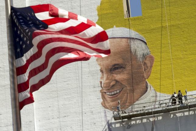 The U.S. flag flies as painters work on a mural of Pope Francis on the side of a building in midtown Manhattan in New York August 28, 2015.