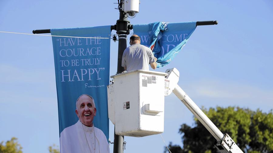 A worker hangs banners last week along the Benjamin Franklin Parkway in Philadelphia before Pope Francis' visit to the city this weekend. (Matt Rourke / AP)