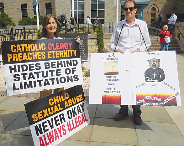 Mirror photo by Kay Stephens / Rosalind Merritts of Hollidaysburg and John Nesbella of Lilly display protest signs outside the Blair County Courthouse after Wednesday’s court hearing on criminal charges filed against three Franciscan friars.