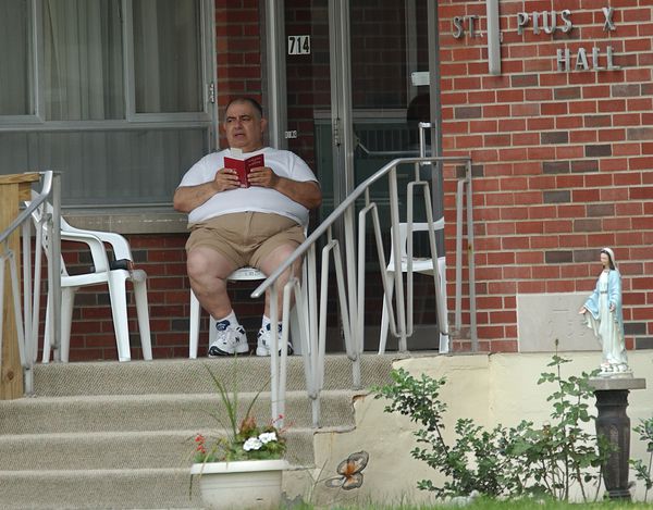 Rev. Chester Misercola pictured in a 2002 file photo reading outside St. Pious X Hall, also known as the Tommy Coyne House, where several priests who were removed from ministry lived before it was shuttered in 2016. Photo by John Berry | The Post-Standard.