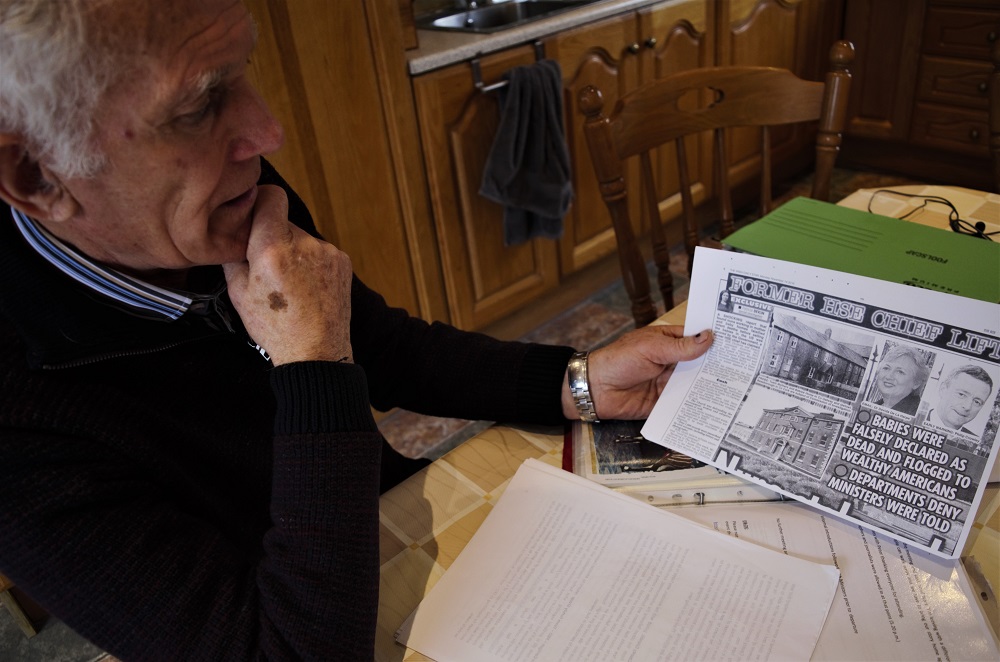 Peter Mulryan reads an article about Irish children who were registered as dead and then sold to Americans, sits at his kitchen table in Ballinasloe, Ireland. Mulryan believes a sister he has never known may have ended up being sold in such a secretive deal. (Photo by CAIN BURDEAU/Courthouse News Service)