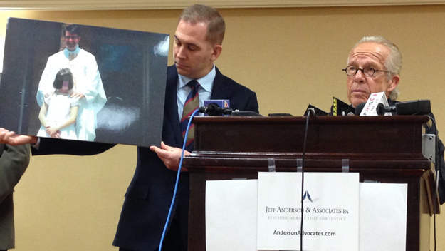 Lawyers John Michael Reck (left) and Jeff Anderson (right) holds photo of Father Gregory Yachyshyn, accused of sexual abuse, with accuser at news conference on Wednesday, Jan. 21, 2015. (Credit: Mona Rivera/1010 WINS)
