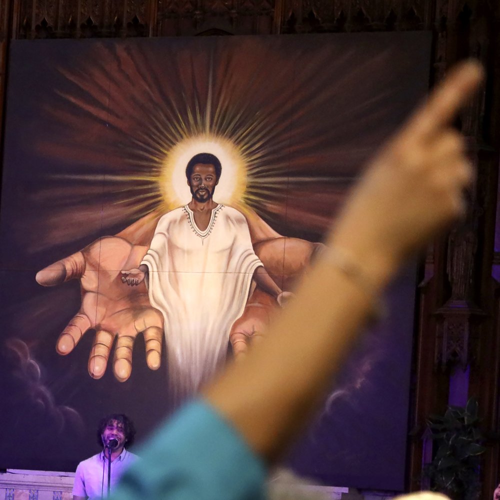 A parishioner raises their hand in front of a painting of Black Jesus during a Sunday church service at St. Sabina Catholic Church in the Auburn Gresham neighborhood in Chicago, Sunday, March 7, 2021. (AP Photo/Shafkat Anowar)