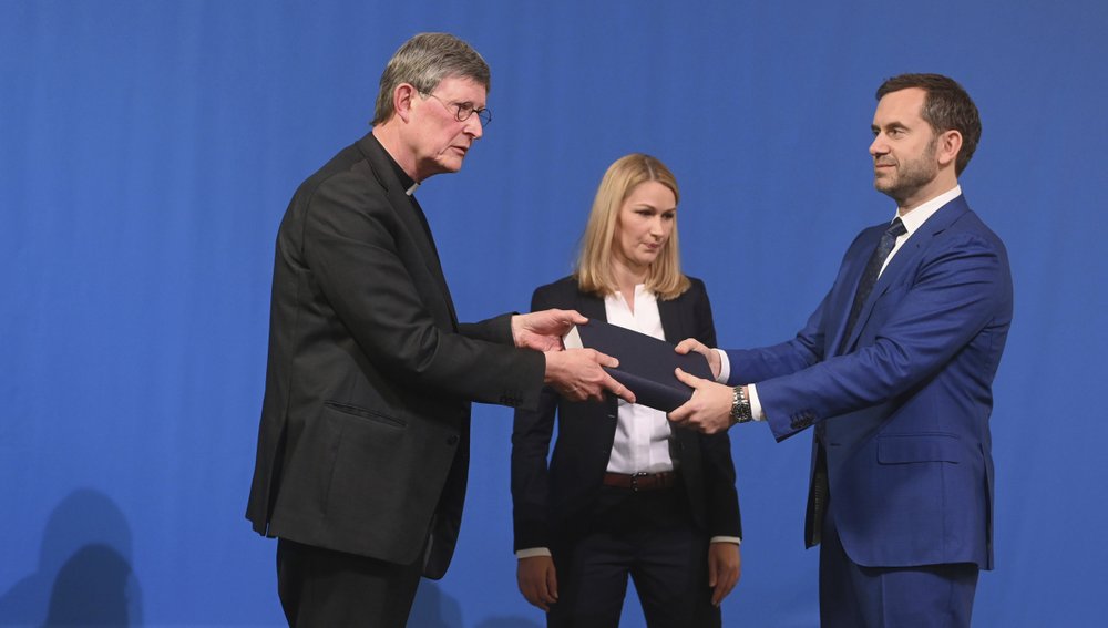 Lawyer Kerstin Stirner, center, looks on as Bjoern Gercke, right, an attorney mandated by the Church, hands over a report on abuse by clergy to Cologne's archbishop Cardinal Rainer Maria Woelki, left, during a news conference in Cologne, Germany, Thursday, March 18, 2021. Faced with accusations of trying to cover up sexual violence in Germany's most powerful Roman Catholic diocese, the archbishop of Cologne publishes the independent investigation. (Ina Fassbender / Pool via AP)