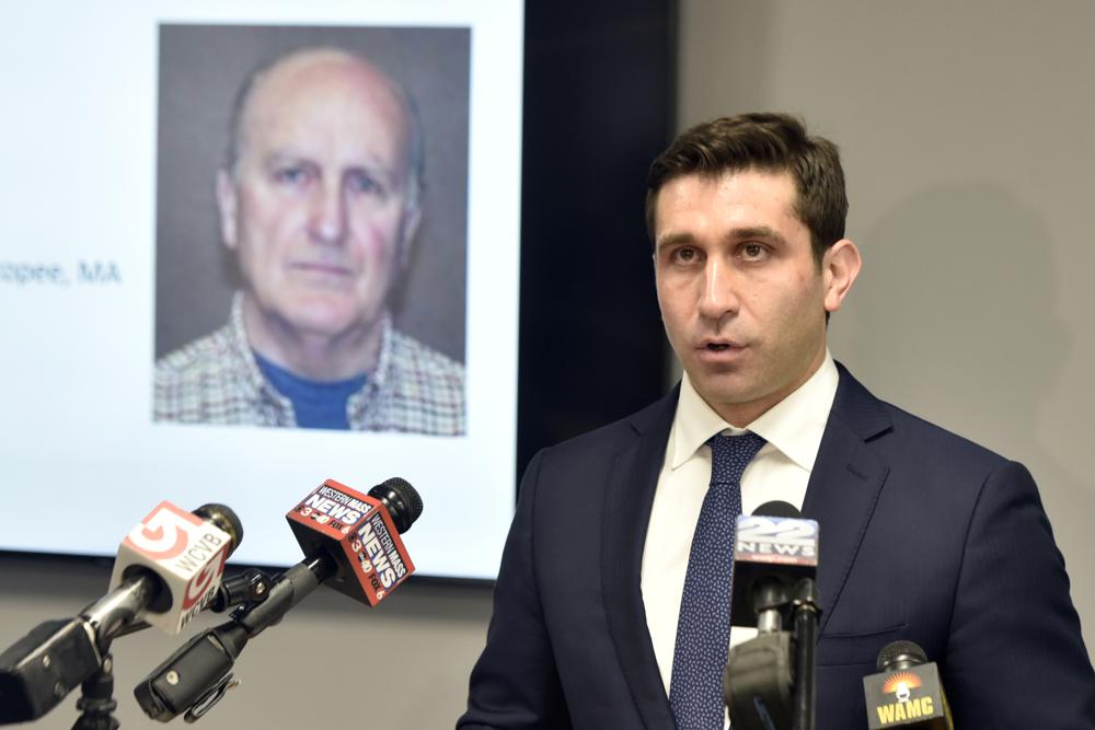 Hampden District Attorney Anthony D. Gulluni, right, speaks during a news conference, Monday, May 24, 2021, in Springfield, Mass., held to announce that defrocked Catholic priest Richard R. Lavigne, pictured on screen at left, was about to be arrested for the 1972 killing of alter boy Daniel Croteau. Investigators were preparing to seek an arrest warrant for the defrocked Roman Catholic priest long considered a suspect in the 1972 killing of a western Massachusetts altar boy shortly before his death last week, a prosecutor said Monday. (Don Treeger/The Republican via AP)