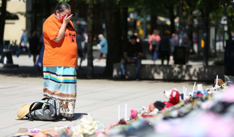 A woman mourns beside 215 pairs of children's shoes outside Vancouver Art Gallery during a memorial in Vancouver, British Columbia, Canada, Saturday, after a mass grave of Indigenous children was found. Photo: Mert Alper Dervis/Anadolu Agency via Getty Images