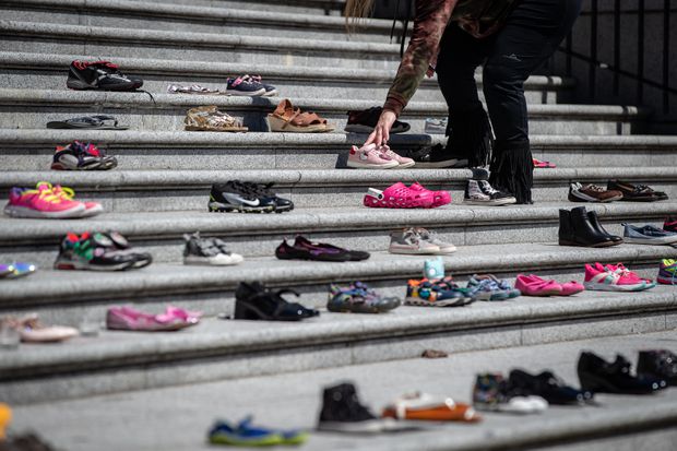 A woman places one of 215 pairs of children's shoes on the steps of the Vancouver Art Gallery as a memorial to the 215 children whose remains have been found buried at the site of a former residential school in Kamloops, in Vancouver, on May 28, 2021.  Darryl Dyck / Canadian Press