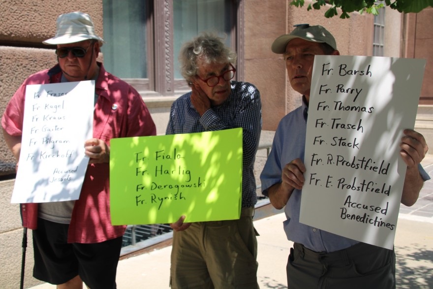 Longtime SNAP members, David Biersmith, Tom White, and David Clohessy hold up signs listing the accused priests' names.