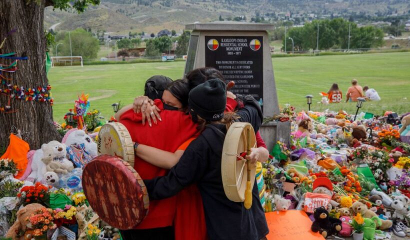 People from Mosakahiken Cree Nation hug in front of a makeshift memorial at the former Kamloops Indian Residential School to honour the 215 children whose remains have been discovered buried near the facility, in Kamloops, British Columbia, Canada, on June 4, 2021. - Canadian Prime Minister Justin Trudeau on June 4 urged the Catholic Church to "take responsibility" and release records on indigenous residential schools under its direction, after the discovery of remains of 215 children in unmarked graves. (Photo by Cole Burston / AFP)