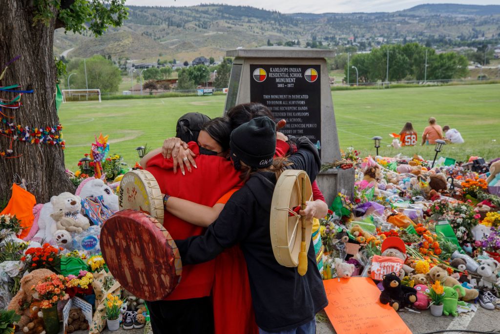 People from Mosakahiken Cree Nation hug in front of a makeshift memorial at the former Kamloops Indian Residential School to honour the 215 children whose remains have been discovered buried near the facility, in Kamloops, British Columbia, Canada, on June 4, 2021. - Canadian Prime Minister Justin Trudeau on June 4 urged the Catholic Church to "take responsibility" and release records on indigenous residential schools under its direction, after the discovery of remains of 215 children in unmarked graves. (Photo by Cole Burston / AFP)