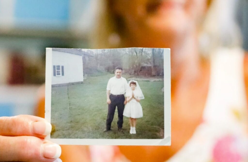 Sheri Biasin, 61, holds a photograph from 1967 of herself at age 7 with her father at her childhood home in West Stockbridge, on the day of her first Communion. Just hours after the photograph was taken, “that little girl’s life changed forever,” Biasin said. That day, Biasin was subjected to the first of what would become a yearslong pattern of sexual abuse by the priest who delivered her Communion.  Stephanie Zollshan - Berkshire Eagle