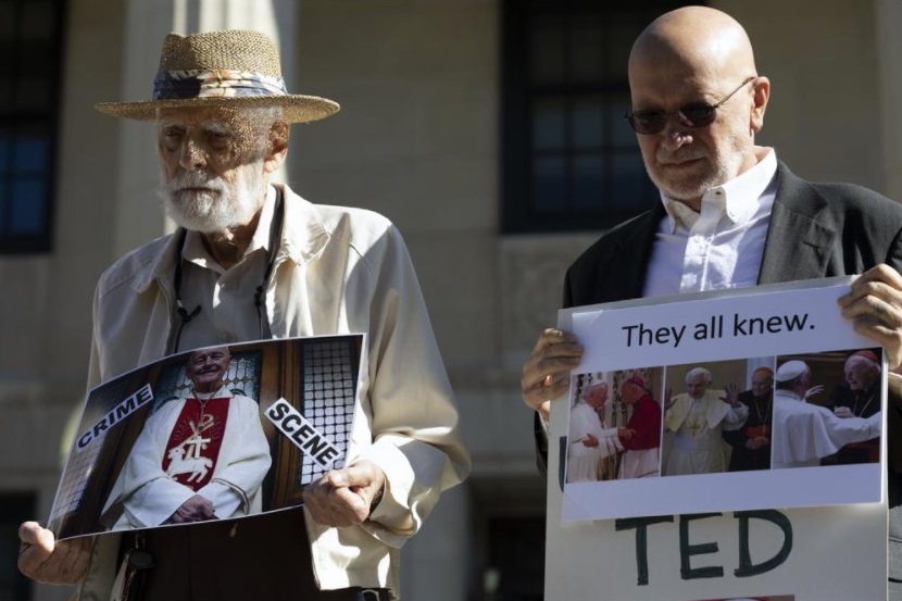 Stephen Sheehan, left, and Skip Shea hold signs during a news conference outside Dedham District Court following the arraignment of former Cardinal Theodore McCarrick, Friday, Sept. 3, 2021, in Dedham, Mass. McCarrick has pleaded not guilty to sexually assaulting a 16-year-old boy during a wedding reception in Massachusetts nearly 50 years ago. (AP Photo / Michael Dwyer)