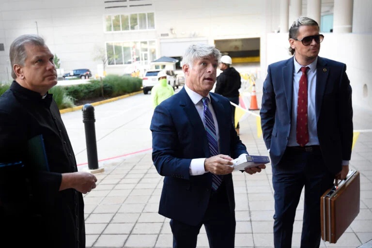 FILE - Fr. Paul Kalchik, from left, St. Michael’s Media founder and CEO Michael Voris, center, and Milo Yiannopoulos talk with a court officer before entering the federal courthouse, Sept. 30, 2021, in Baltimore. A federal judge has blocked Baltimore city officials from banning the conservative Roman Catholic media outlet from holding a prayer rally at a city-owned pavilion during a U.S. bishops’ meeting in November. U.S. District Judge Ellen Hollander ruled late Tuesday, Oct. 13, 2021, that St. Michael’s Media is likely to succeed on its claims that the city discriminated against it on the basis of its political views and violated its First Amendment free speech rights. (AP Photo/Gail Burton, file)