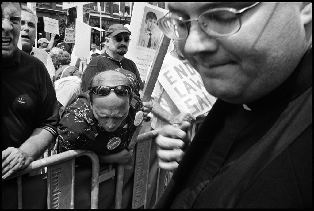 Lisa Kessler, "Wrath" (2003). Several enraged survivors and demonstrators pretend to spit at priests leaving the Mass of Installation for Archbishop Sean O'Malley, Cardinal Bernard Law's successor. Boston, July 2003. ©LISA KESSLER, COURTESY HOWARD YEZERSKI GALLERY