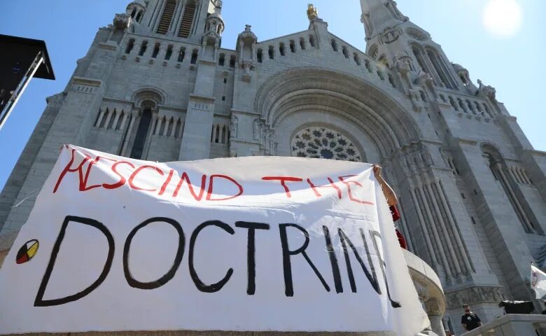 A 'Rescind the doctrine' banner is unfurled outside the Sainte-Anne-de-Beaupré Basilica while Pope Francis held mass Thursday. (Olivia Laperrière-Roy/CBC/Radio-Canada)