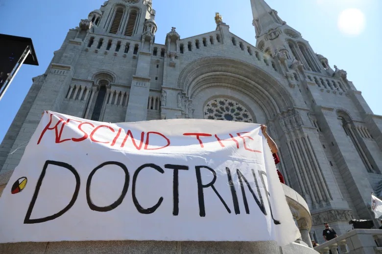 A 'Rescind the doctrine' banner is unfurled outside the Sainte-Anne-de-Beaupré Basilica while Pope Francis held mass Thursday. (Olivia Laperrière-Roy/CBC/Radio-Canada)